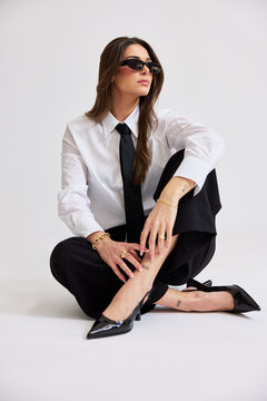 Woman in black and white outfit sits on floor with sunglasses