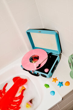 a blue record player spins a pink vinyl beside a bathtub with floaties