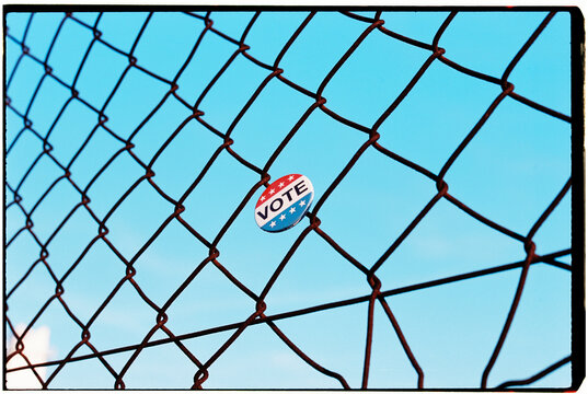 a vote badge is caught in a wire fence against a blue sky, 35mm film