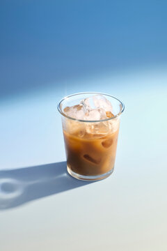 Refreshing iced coffee with milk and ice cubes in clear glass on blue