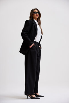 Woman in black suit poses confidently against plain background