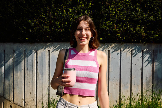 Happy woman stands on the street, carrying a takeaway cup