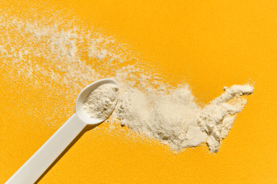 White powder supplement in measuring scoop spilled on yellow table