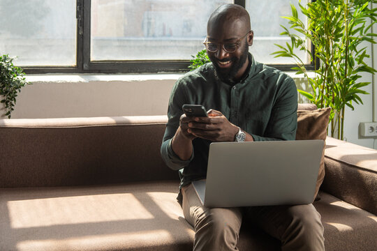 Smiling Man Working  On Laptop While Texting On His Phone