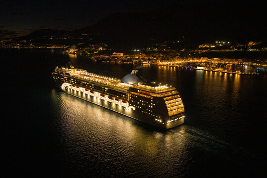 Cruise Ship Sails at Night Near a Coastal Town With Lights Shining