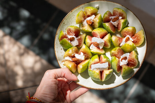 Hand holding a plate of fresh figs stuffed with cheese and almonds