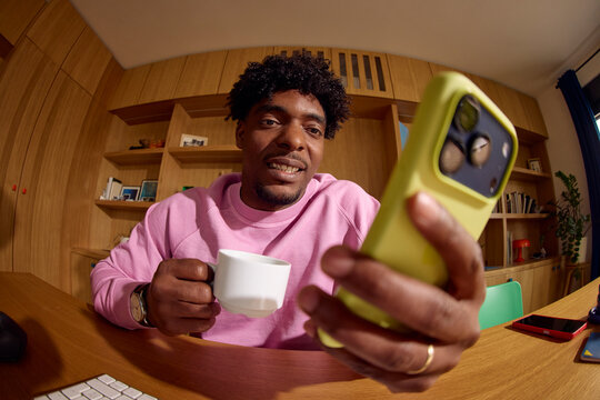 Man sips coffee at home while checking his phone.