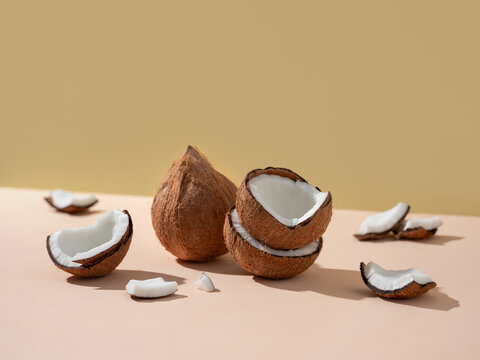 Coconuts, whole and cracked, arranged on a light pink background