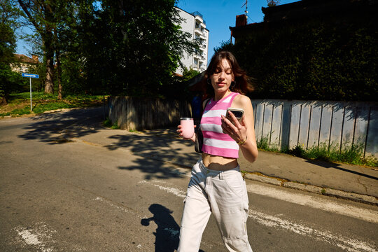 Casual young woman crosses the street, looking at a mobile phone