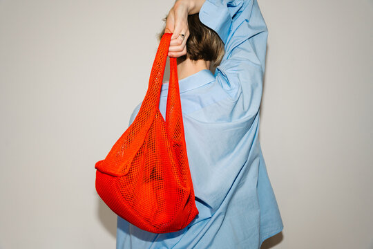 Woman holding bright mesh bag from behind