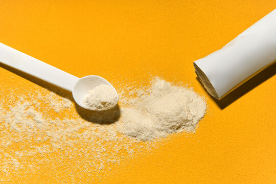 White powder supplement spilled on yellow table with scoop. 