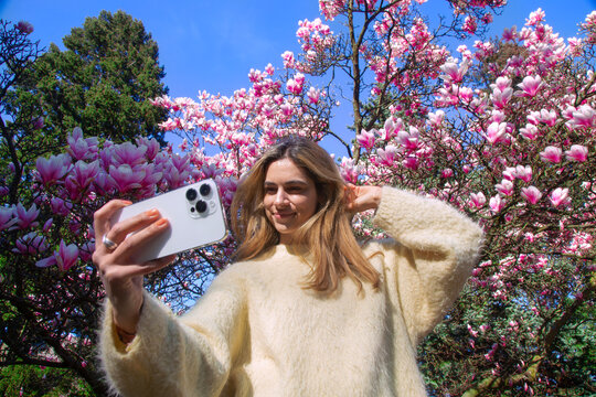 A woman taking selfies in front of a cherry blossom tree
