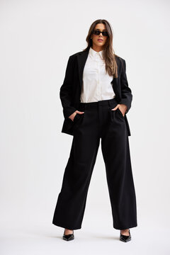 Woman stands confidently in black suit and sunglasses indoors