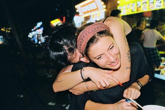 Friends laughing and hugging at night food stalls