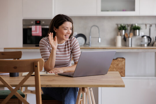 Woman Waves During Video Call over her lapto in Modern Kitchen at Home