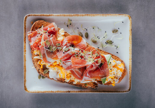 Open sandwich with prosciutto, scrambled egg and shoots