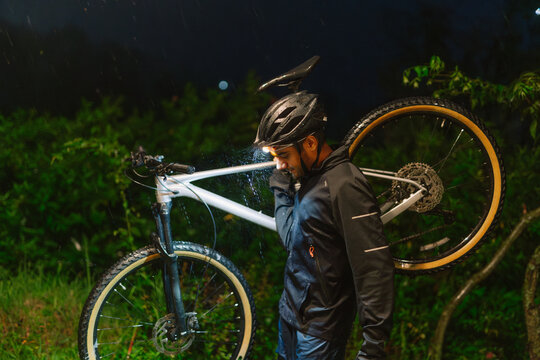Cyclist Walks With Bicycle in the Rain at Night in the Park
