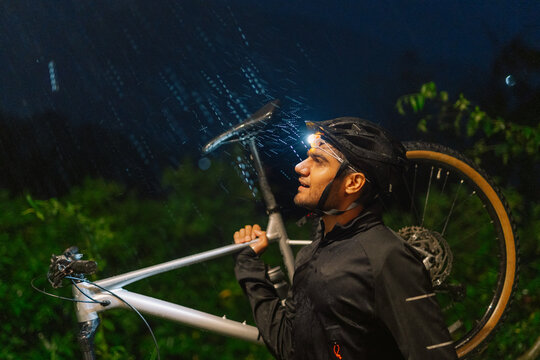 Cyclist Carries Bike While Walking in Rain at Night