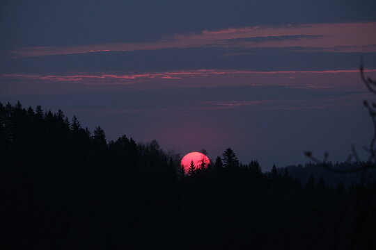 Golden sunrise over dark forest and mountains.