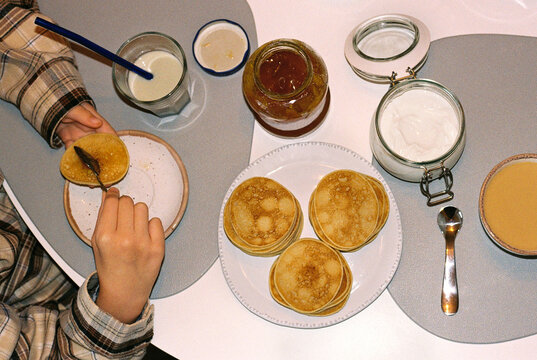 Anonymous girl spreads jam on a pancake during breakfast.