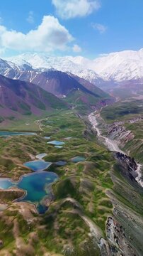 Aerial view of Tulpar Lake and turquoise alpine ponds nestled among green hills and winding riverbeds with snow-capped mountains in Alay District, Osh Region, Kyrgyzstan.