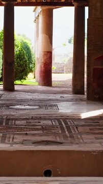 Vertical view across a preserved Pompeii atrium floor with geometric mosaic tiles, circular basin holes, columns, warm sunlight, and ancient Roman interior details.