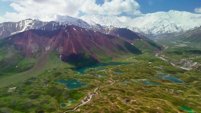 Aerial view of Tulpar Lake surrounded by green hills and turquoise ponds with snow-capped peaks in the background, Alay District, Osh Region, Kyrgyzstan.