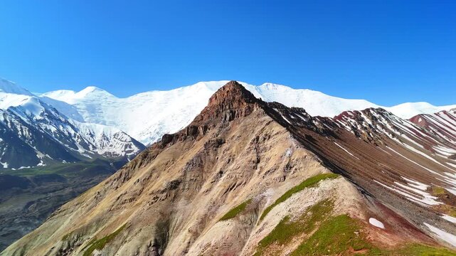 Aerial view of Base Camp for Peak Lenin area with colorful ridges and snow-capped Pamir Mountains under a clear blue sky in Chong-Alay District, Osh Region, Kyrgyzstan.
