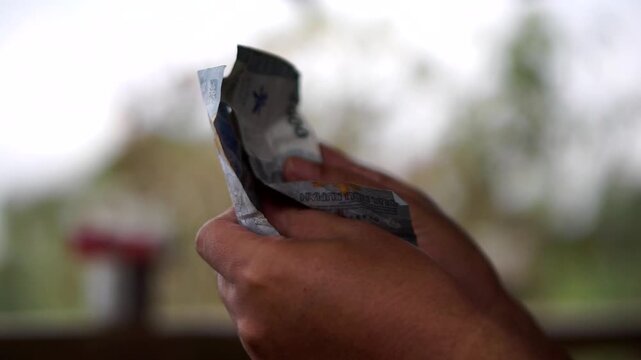Close-up of a person's hands counting crumpled two thousand Indonesian Rupiah banknotes.