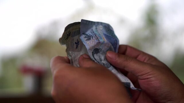 Close-up of a person's hands counting crumpled two thousand Indonesian Rupiah banknotes.