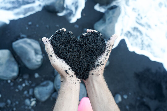 Person cupping black sand in heart shape at Hawaiian black sand beach