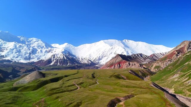 Aerial view of Base Camp for Peak Lenin with snow-capped mountain peaks and green valley under a clear blue sky in Chong-Alay District, Osh Region, Kyrgyzstan.