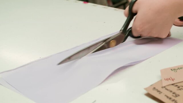 Professional sewing. Cutting garment. Woman working with scissors on studio table. Tailor hand creating clothes with cardboard draft.