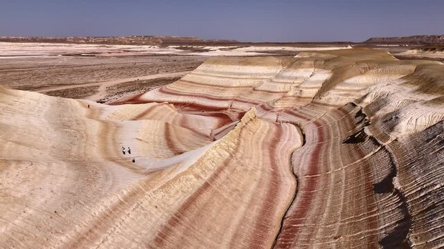 Aerial view of the colorful layered rock formations of Kyzylkum with people walking along the ridges in the desert landscape Kyzylkum, Mangystau Region, Kazakhstan.