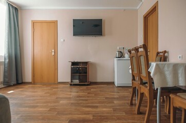 Fototapeta premium cozy hotel dining area with a wooden table and four chairs. A small refrigerator and kettle are visible. The walls are painted in soft colors, creating a welcoming atmosphere.
