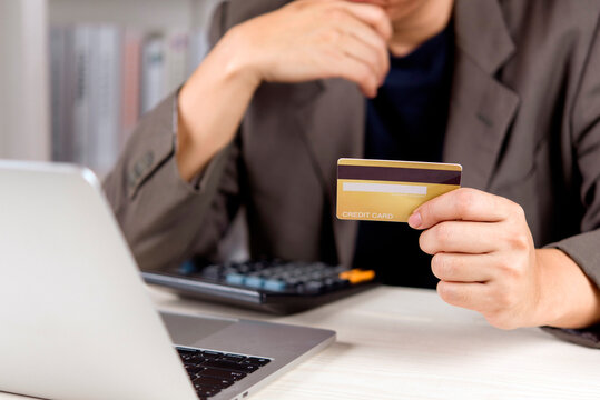 businessman hands holding credit card and looking at laptop on desk. Online shopping, e-commerce payment, financial decision and corporate business transaction budget concept.