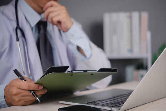Doctor hand holding pen clipboard thinking medical research analysis desk. Healthcare management administration auditing clinical trial documentation professional physician working laptop.