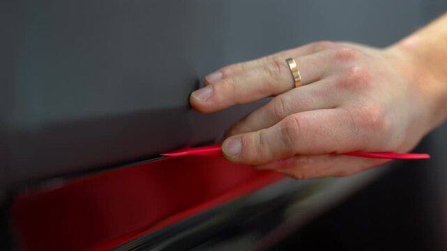 Close up view of a cutting matte vinyl wrap on a car body in a workshop. Automotive detailing process