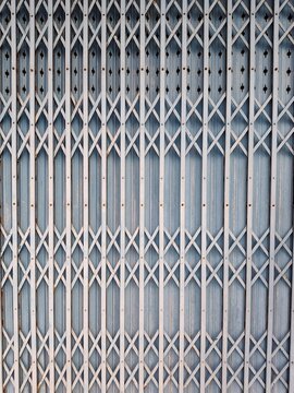 A full frame background texture showing a traditional blue vintage folding metal gate, commonly used as a secure shutter door for shops and storefronts.