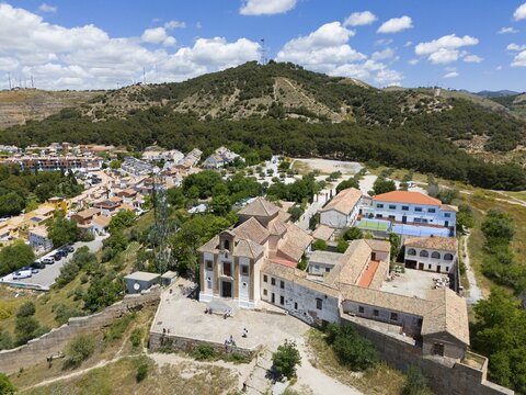 Image of a town with a church in front of a wooded hill under a blue sky with clouds, Ermita de San Miguel Alto, Hermitage of San Miguel, Granada, Andalusia, Spain