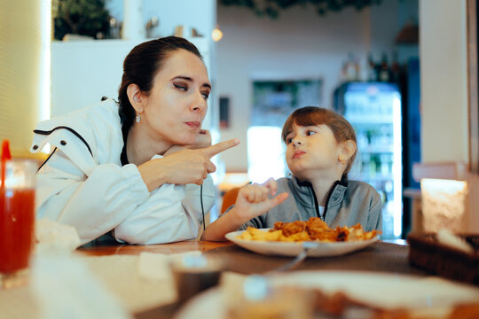 Mother Pointing Finger At Daughter Eating Rudely With her Hands. Mom being upset with her impolite little girl scolding her