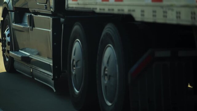 Close up of a semi truck wheels, axle, fuel tank, and chassis in motion. Detailed view of heavy duty trucking transport on the road