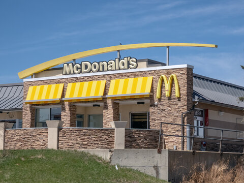 Calgary, Alberta, Canada. June 1, 2026. Exterior McDonald's restaurant stone facade with golden arches sign, eye level view.