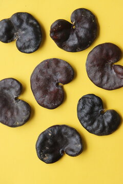 A collection of hard, dark brown Enterolobium contortisiliquum (Earpod tree) seeds, famously known for their distinct ear-like or kidney-shaped appearance. The textured botanical specimens are scatter