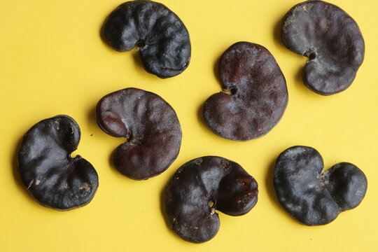 A collection of hard, dark brown Enterolobium contortisiliquum (Earpod tree) seeds, famously known for their distinct ear-like or kidney-shaped appearance. The textured botanical specimens are scatter