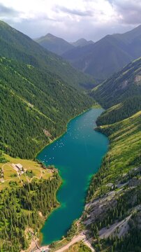Aerial view of Kolsai Lake with turquoise water and small boats surrounded by steep forested mountains in Kegen District, Almaty Region, Kazakhstan.