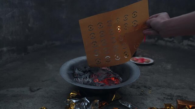 Burning ritual paper offerings in metal basin during traditional ancestor ceremony
