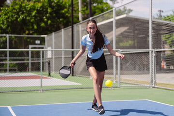 Obraz premium Pickleball sports player, active woman reaching to hit ball on court. Fitness exercise and healthy lifestyle recreation game with dynamic action.