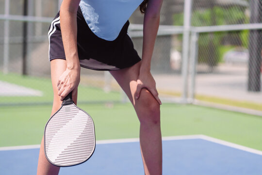 Pickleball sports player resting on outdoor court. Tired female athlete holding paddle and bending knees during fitness training.