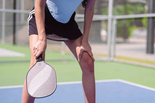 Pickleball sports player resting on outdoor court. Tired female athlete holding paddle and bending knees during fitness training.